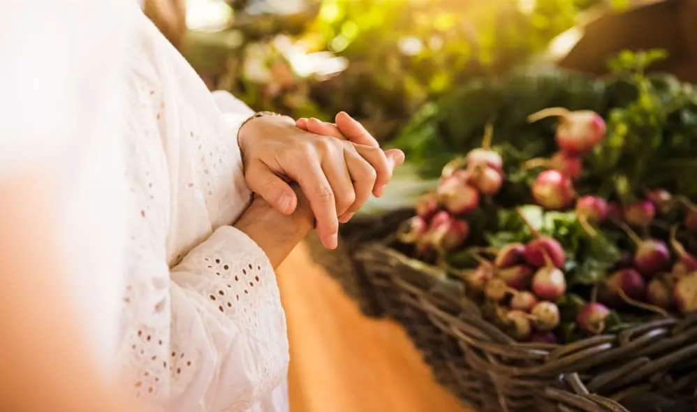 Manos de una mujer vestida de blanco frente a una cesta con frutas frescas en un mercado