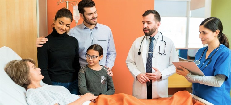 Mujer en cama de hospital sonriente y hablando con el médico y enfermera, su familia junto a ella